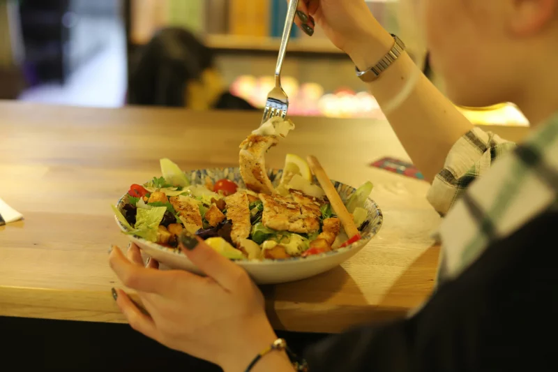 Close-up of a person enjoying a fresh chicken salad at a wooden table indoors.