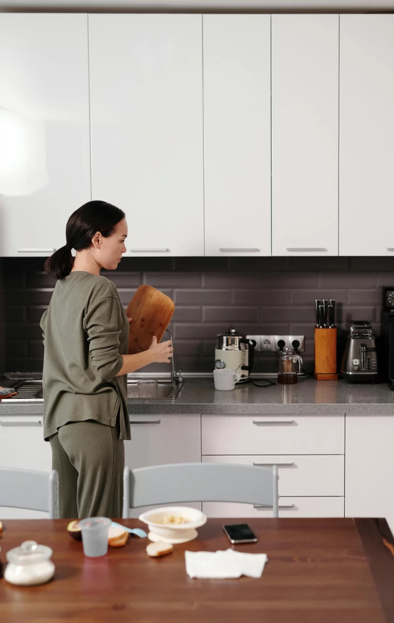 A woman stands in a modern kitchen holding a chopping board, preparing a meal.
