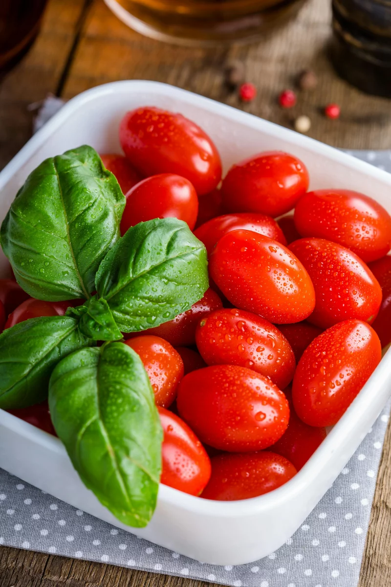 A bowl of vibrant cherry tomatoes garnished with fresh basil leaves on wooden background.