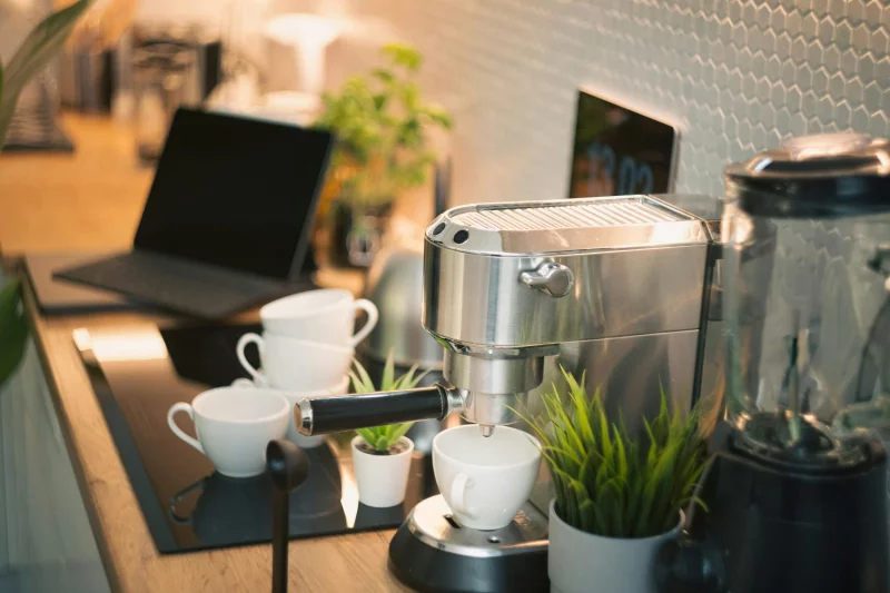 Cozy kitchen counter featuring an espresso machine, laptop, and potted plants in modern design.