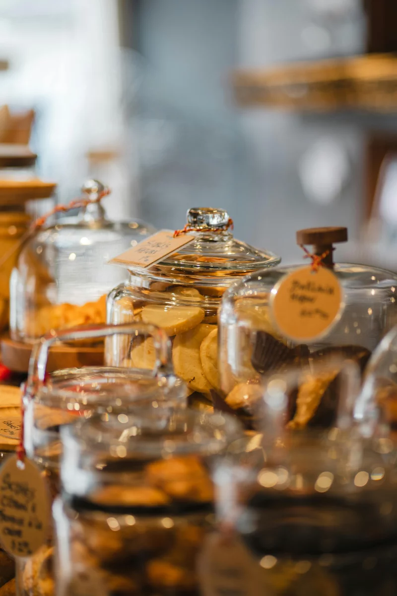 A variety of bakery items displayed in glass jars on a wooden counter inside a store.