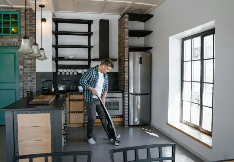 A man cleaning the modern kitchen with a vacuum cleaner, showcasing contemporary interior design.