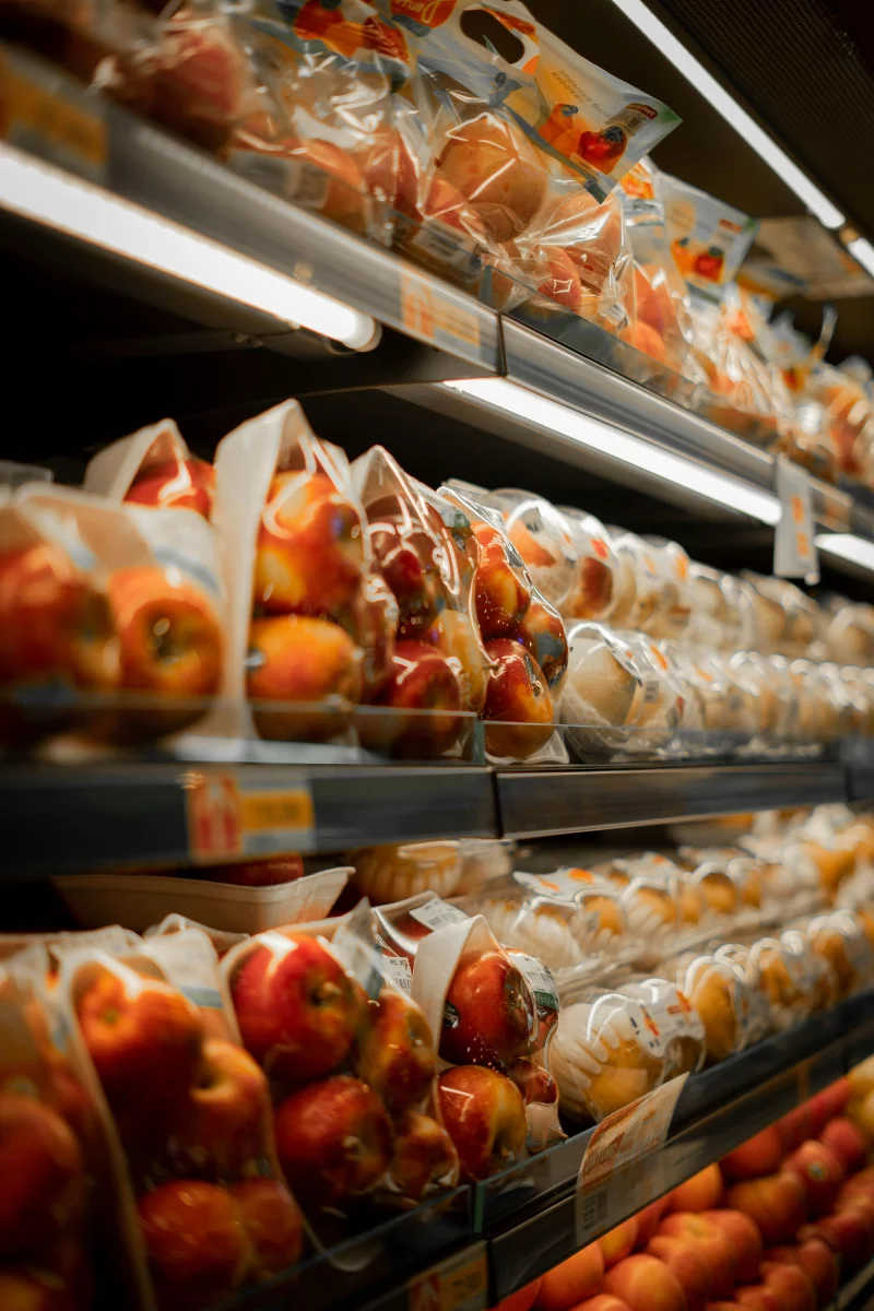 Packaged fresh apples displayed on a supermarket shelf with bright lighting.