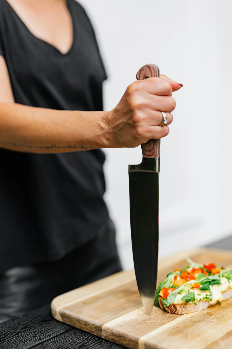 Woman slicing a vibrant vegetable sandwich on a wooden board.