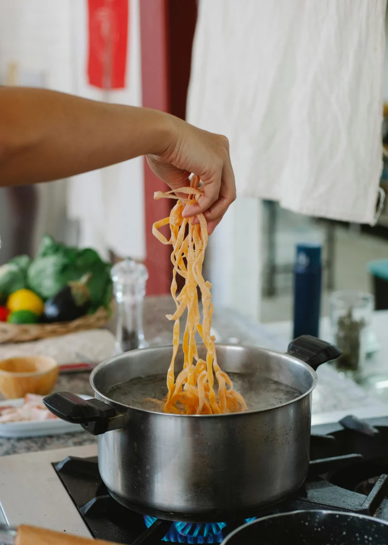 Close-up of a hand cooking fresh pasta in a pot on a gas stove in a modern kitchen.