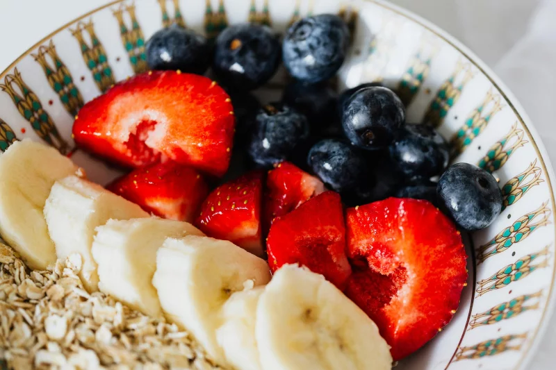 A close-up of a breakfast bowl filled with fresh strawberries, blueberries, banana slices, and oats.