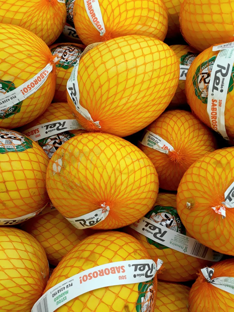 A vibrant collection of fresh yellow melons encased in protective netting, ready for sale.