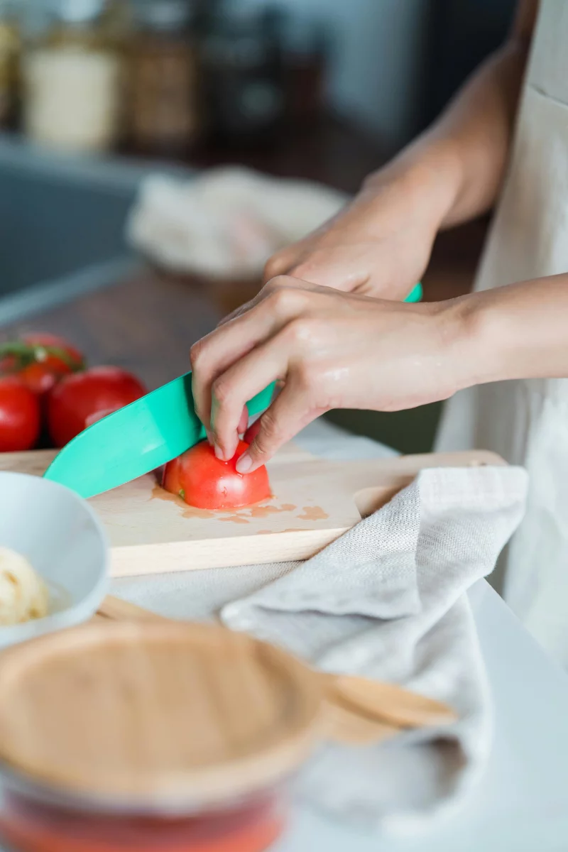 Close-up of hands cutting fresh tomatoes on a wooden board with a knife in a contemporary kitchen.