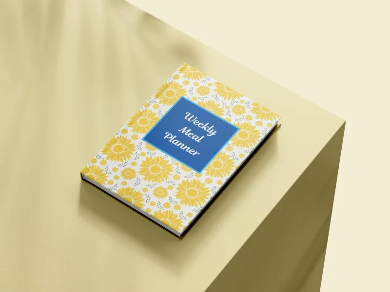 Weekly meal planner book with a floral cover on a minimalist surface, viewed from above.