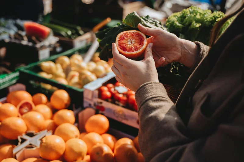 A close-up of a person holding a sliced orange at an outdoor market, showcasing fresh produce.