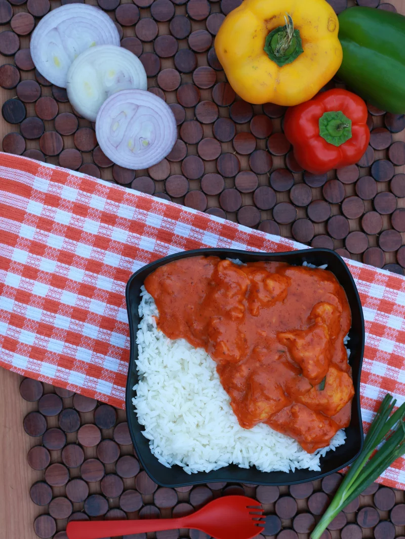 Delicious South Asian curry served with rice, surrounded by fresh vegetables and rustic elements.