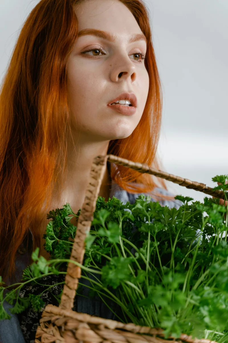 Portrait of a young woman holding a basket of fresh parsley in a studio setting.