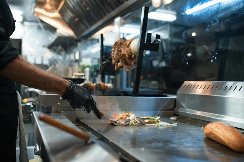 A chef prepares grilled meat and vegetables in a professional kitchen setting.