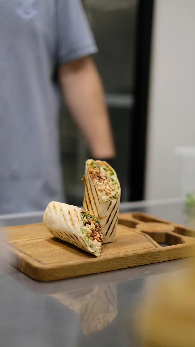 Appetizing grilled burrito on a cutting board in the kitchen with a blurred person in the background.