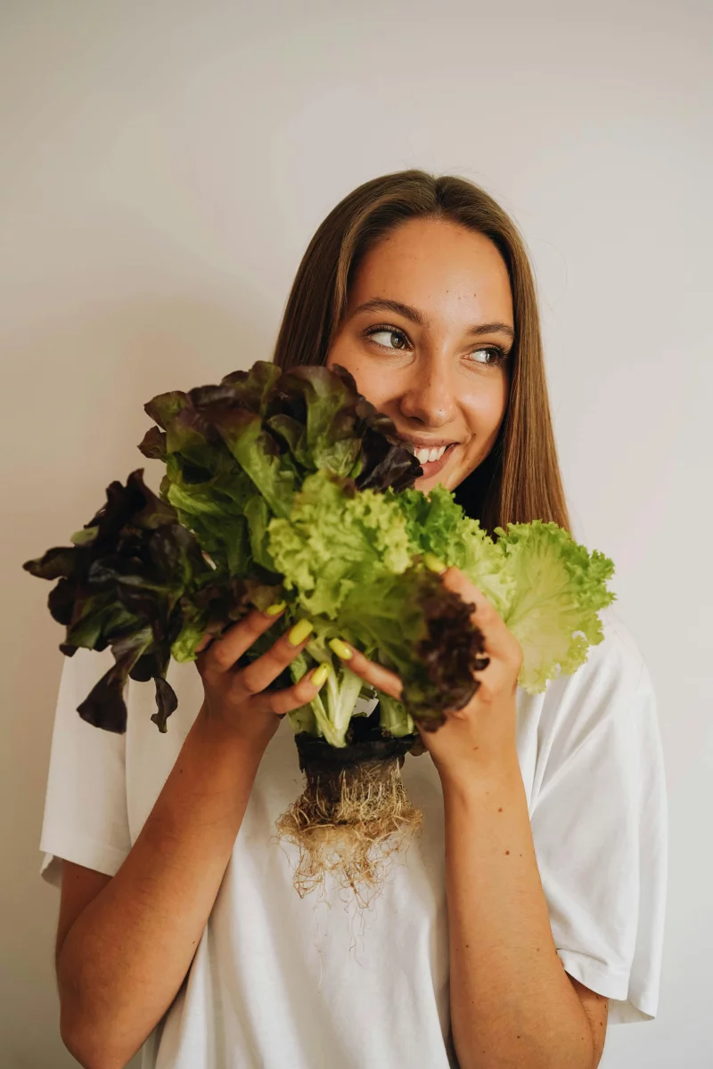 Happy woman holding fresh lettuce against a light wall, showcasing healthy lifestyle and fresh produce.