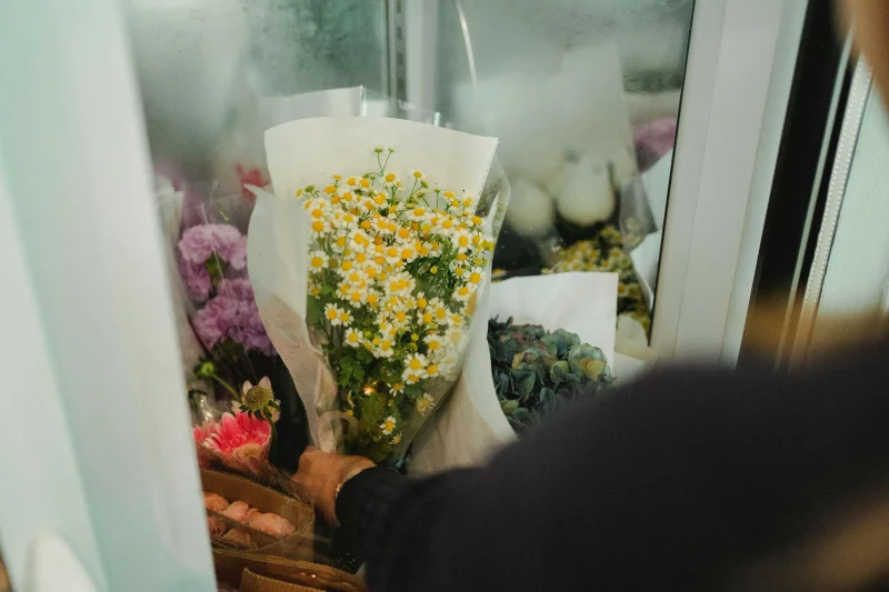 Crop faceless female florist putting bouquets of flowers in fridge while working in floral shop