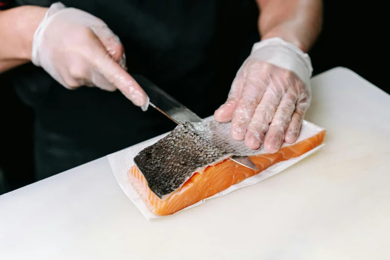 Close-up of a chef skillfully skinning a fresh salmon fillet using a knife.