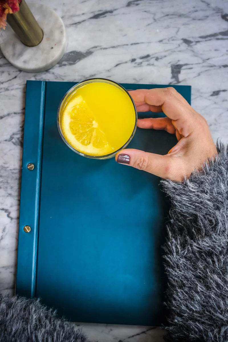 A hand holding orange juice over a blue notebook, evoking a cozy and refreshing vibe.