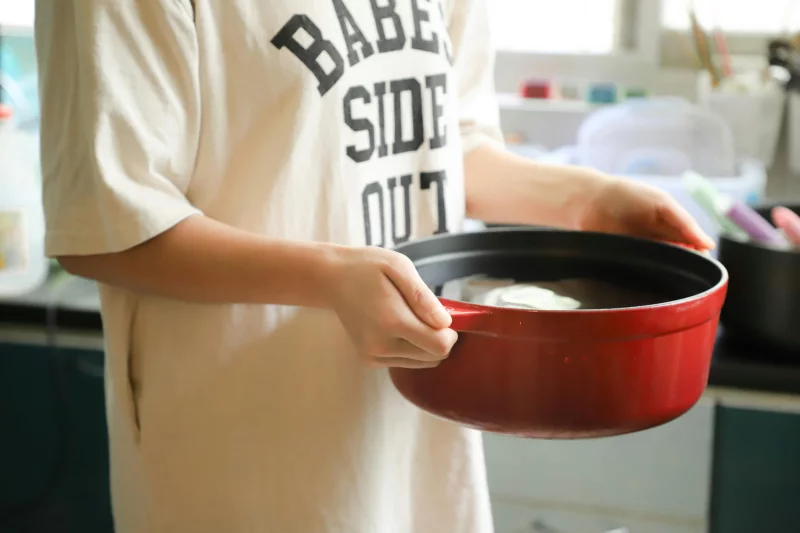 Close-up of individual holding red cooking pot, preparing food indoors.