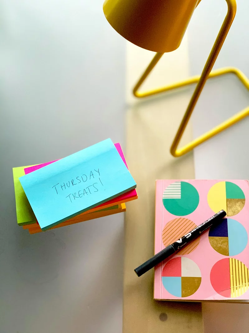 Bright and colorful office desk setup featuring sticky notes, a decorative notebook, and a modern yellow lamp.