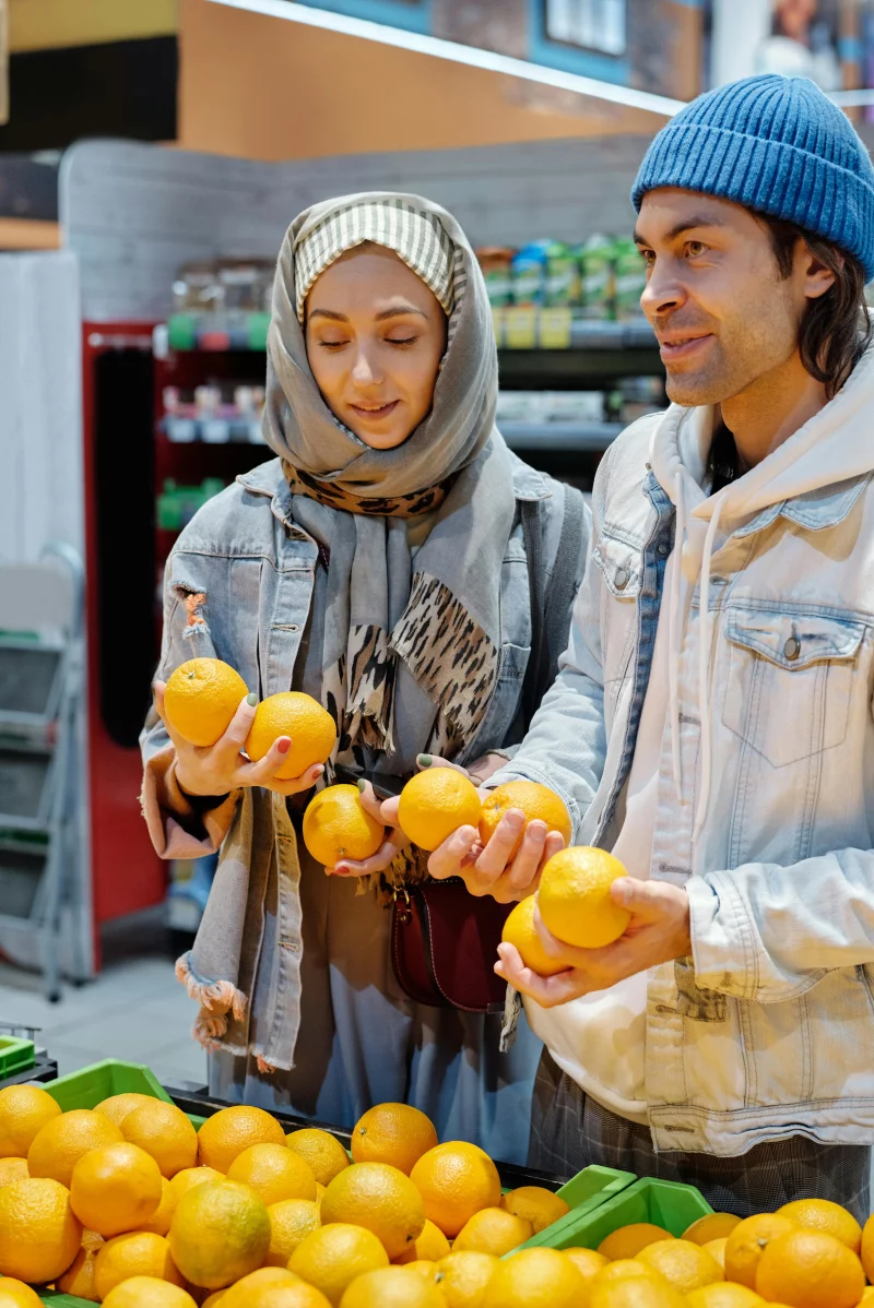 Man and woman selecting oranges in a supermarket, focused on quality and freshness.