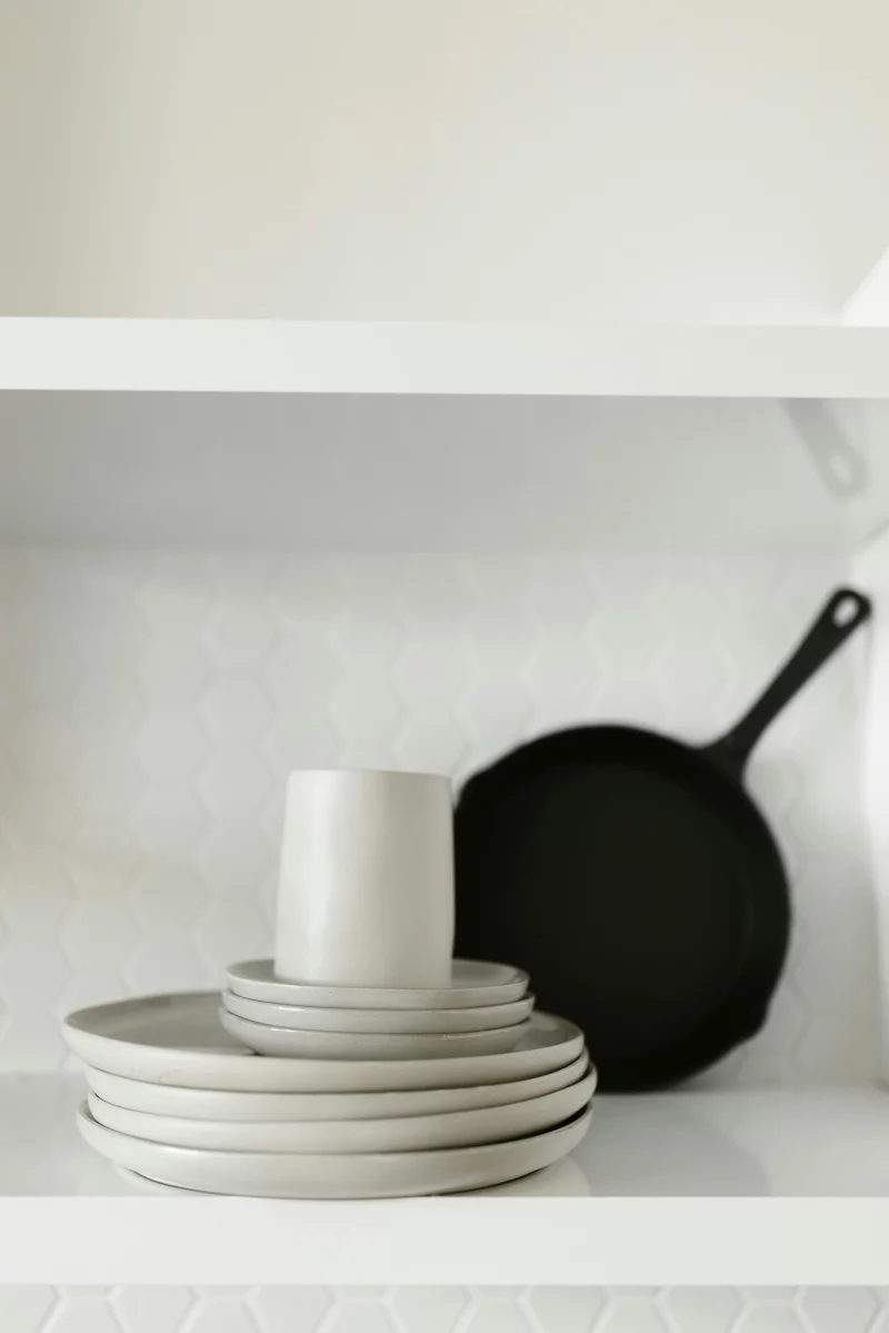 Ceramic dinnerware and black frying pan on a minimalist kitchen shelf.