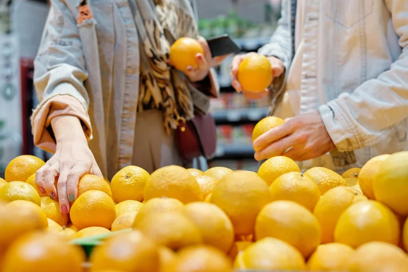 Close-up of hands selecting fresh oranges in a bustling market.