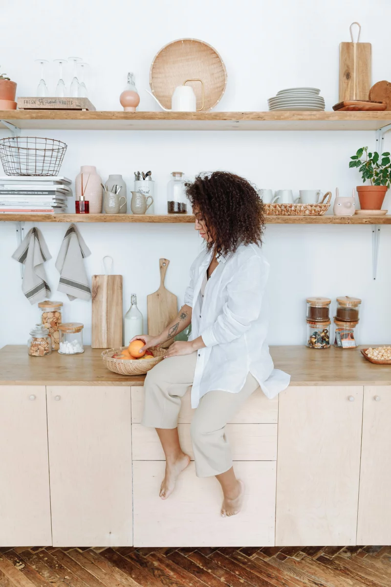 Woman sitting on a kitchen counter arranging fruit, creating a cozy and organized kitchen space.