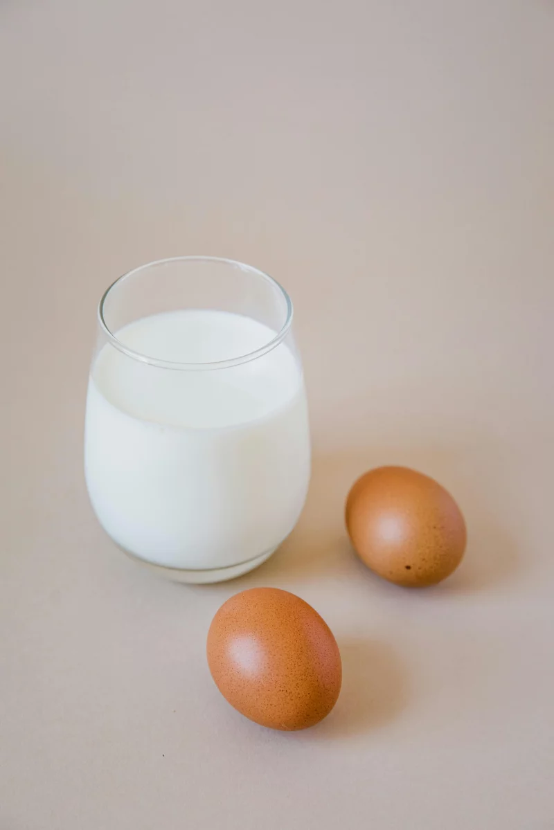 A simple composition featuring a glass of milk and two brown eggs on a beige background.