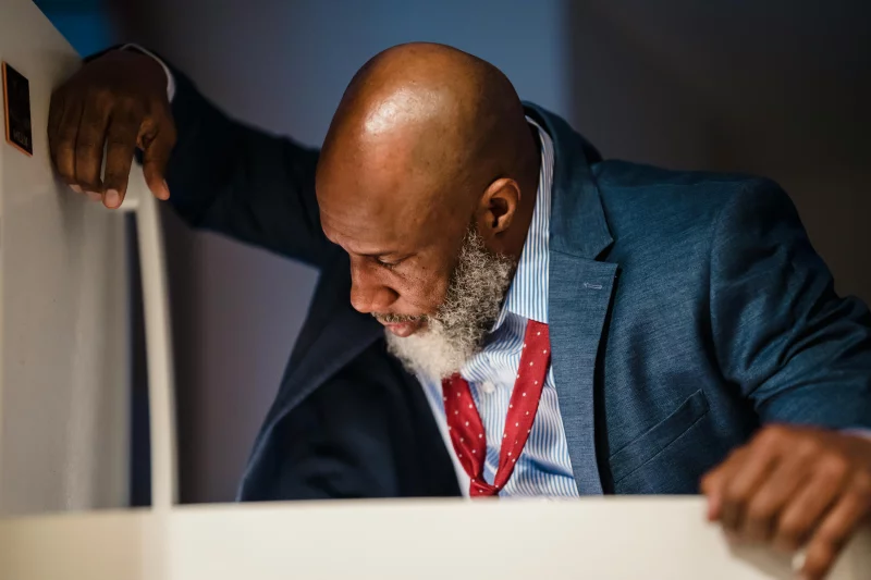 An adult man in a suit looks into an office refrigerator during the daytime.