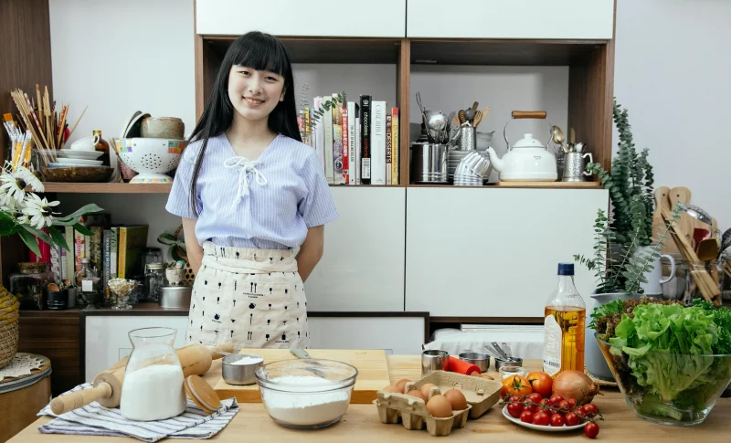 Asian woman smiling in a modern kitchen with fresh ingredients prepped for cooking.