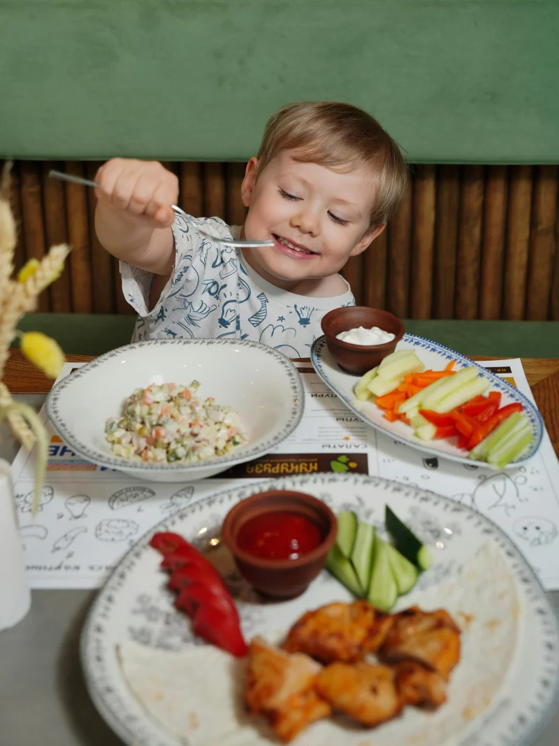 Smiling child eating a healthy meal with fresh vegetables at home. Joyful dining experience.