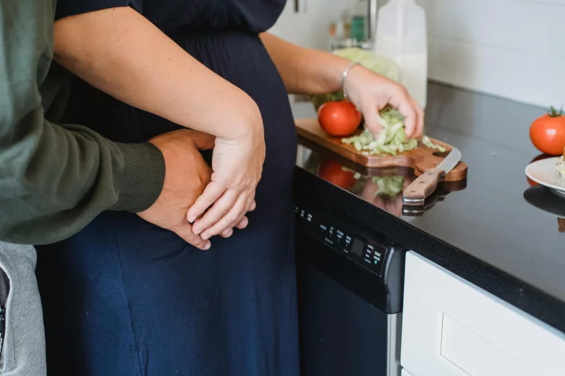 A couple embraces in the kitchen while preparing a fresh salad, symbolizing love and healthy living.