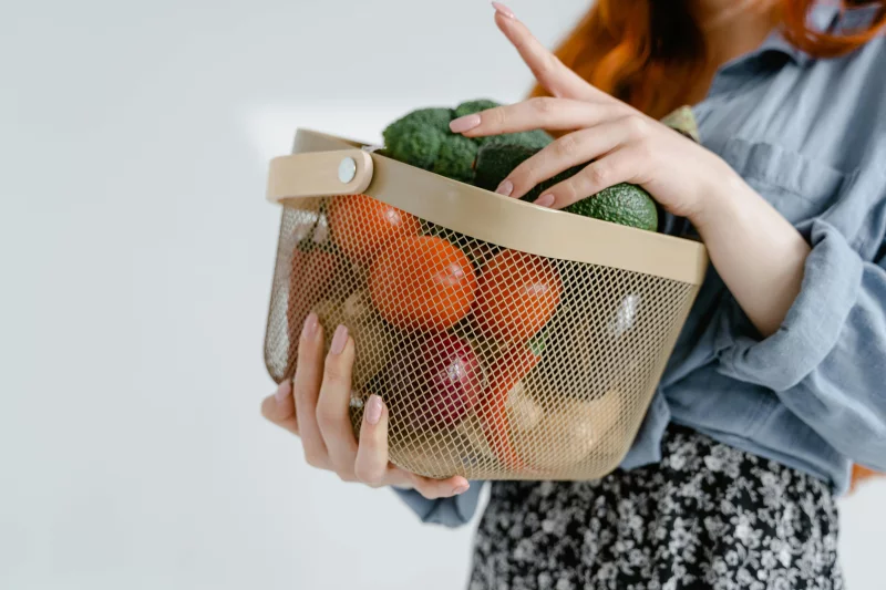 Close-up of a person holding a basket filled with fresh vegetables, symbolizing healthy living.