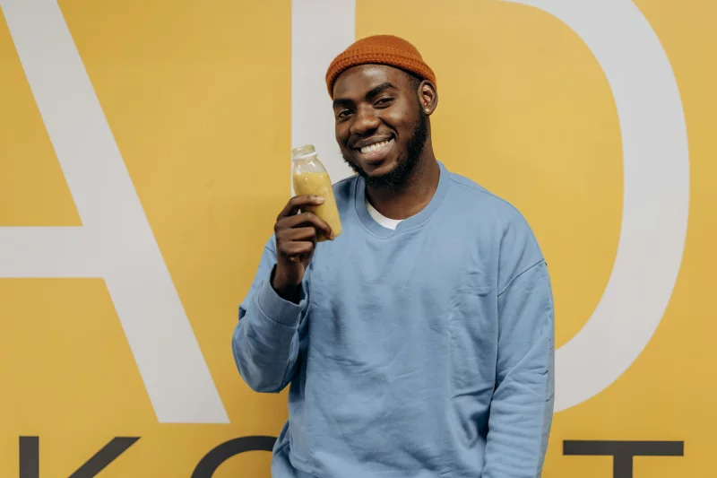 Happy man in blue sweater holding a nutritious drink against a yellow background.