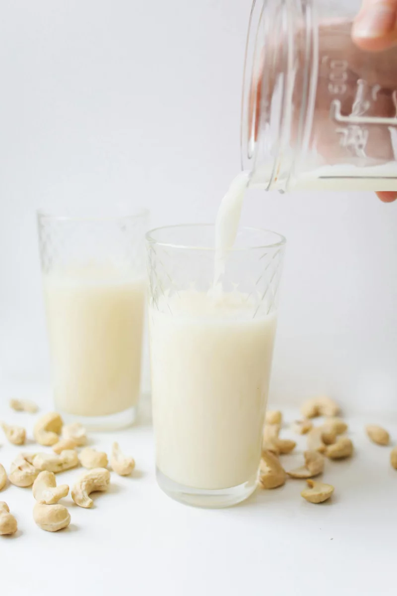 Delicious cashew milk being poured into a glass surrounded by cashews, showcasing refreshing plant-based nutrition.