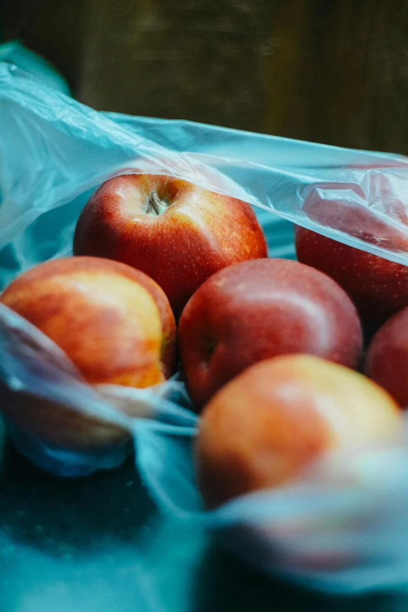A detailed close-up of fresh apples captured inside a transparent plastic bag on a dark surface.