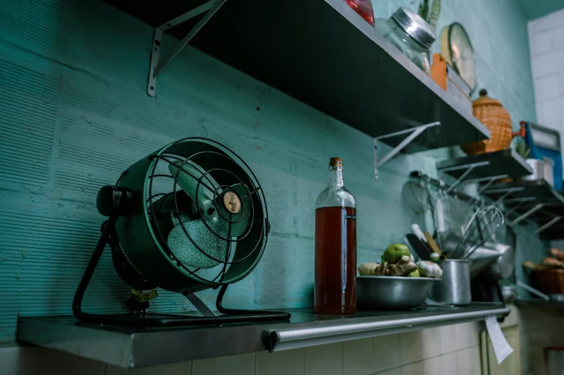 A rustic kitchen scene featuring a vintage fan, cookware, and open shelves, evoking a retro Brazilian style.