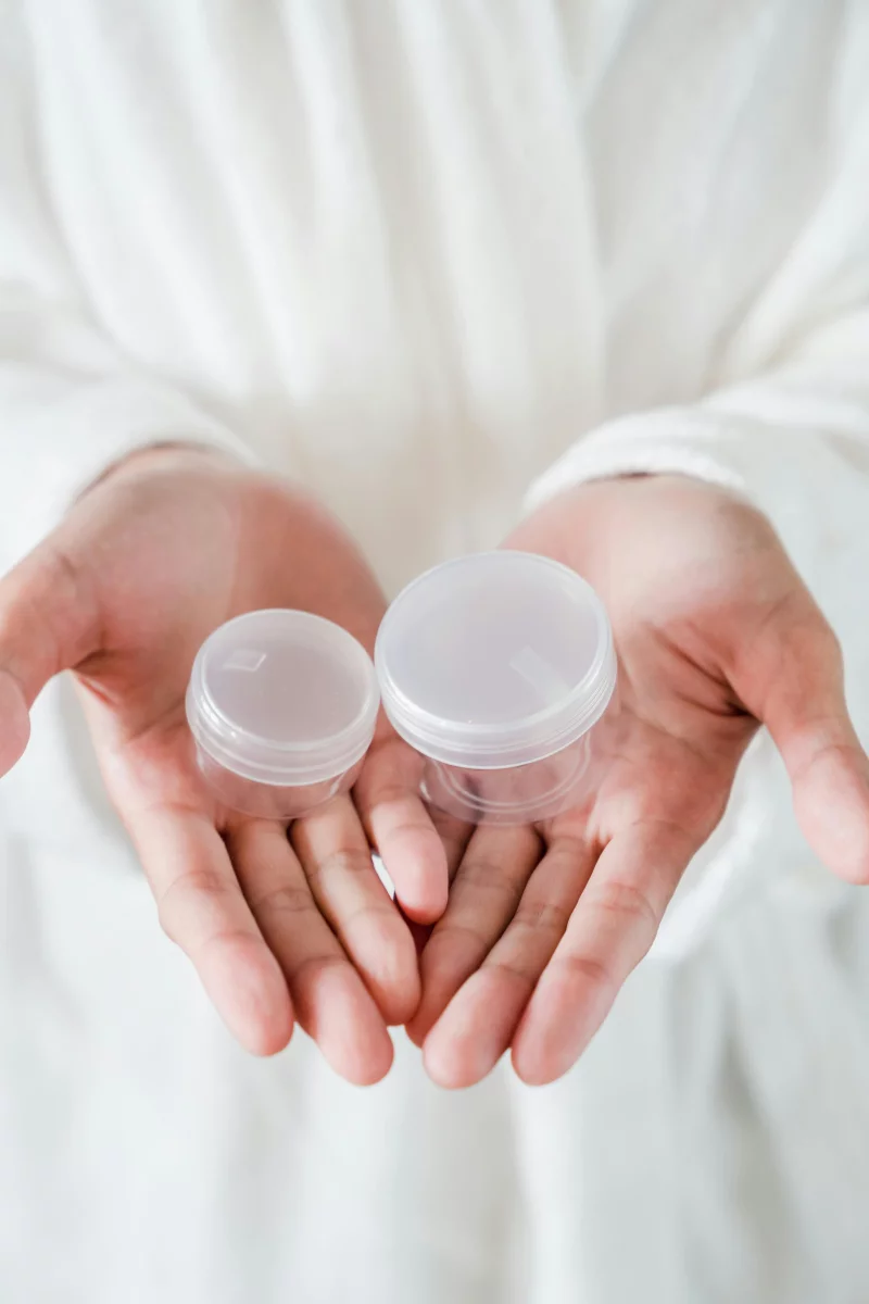 Close-up of hands holding two small clear plastic containers.