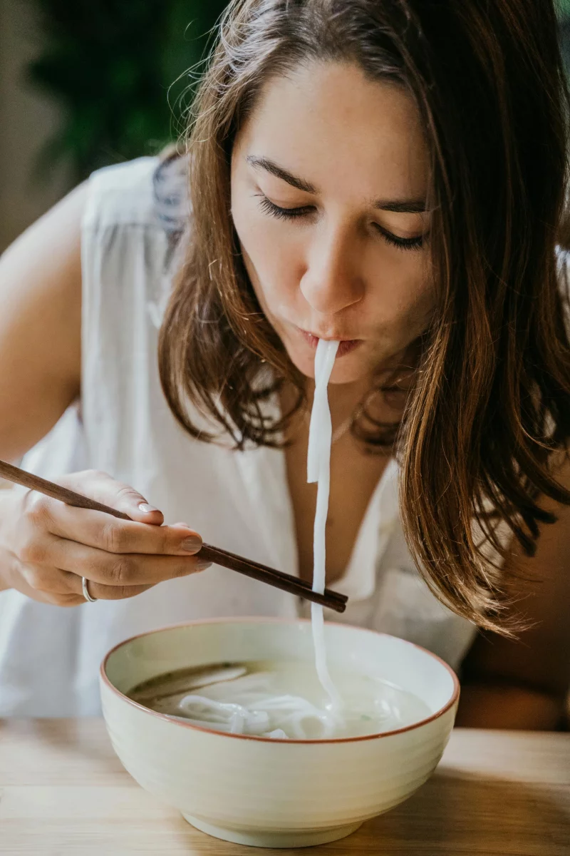 Young woman eating noodle soup with chopsticks in a close-up shot, enjoying Asian cuisine.
