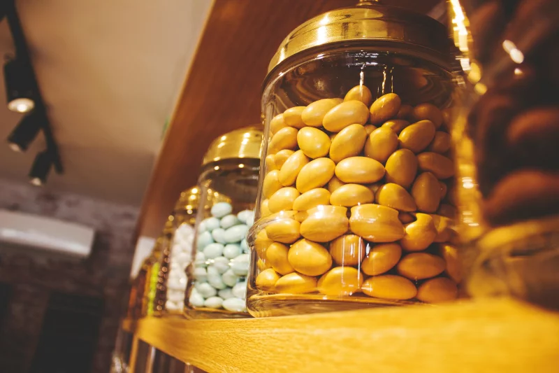 Close-up of assorted candy jars on a wooden shelf in a cozy indoor setting.