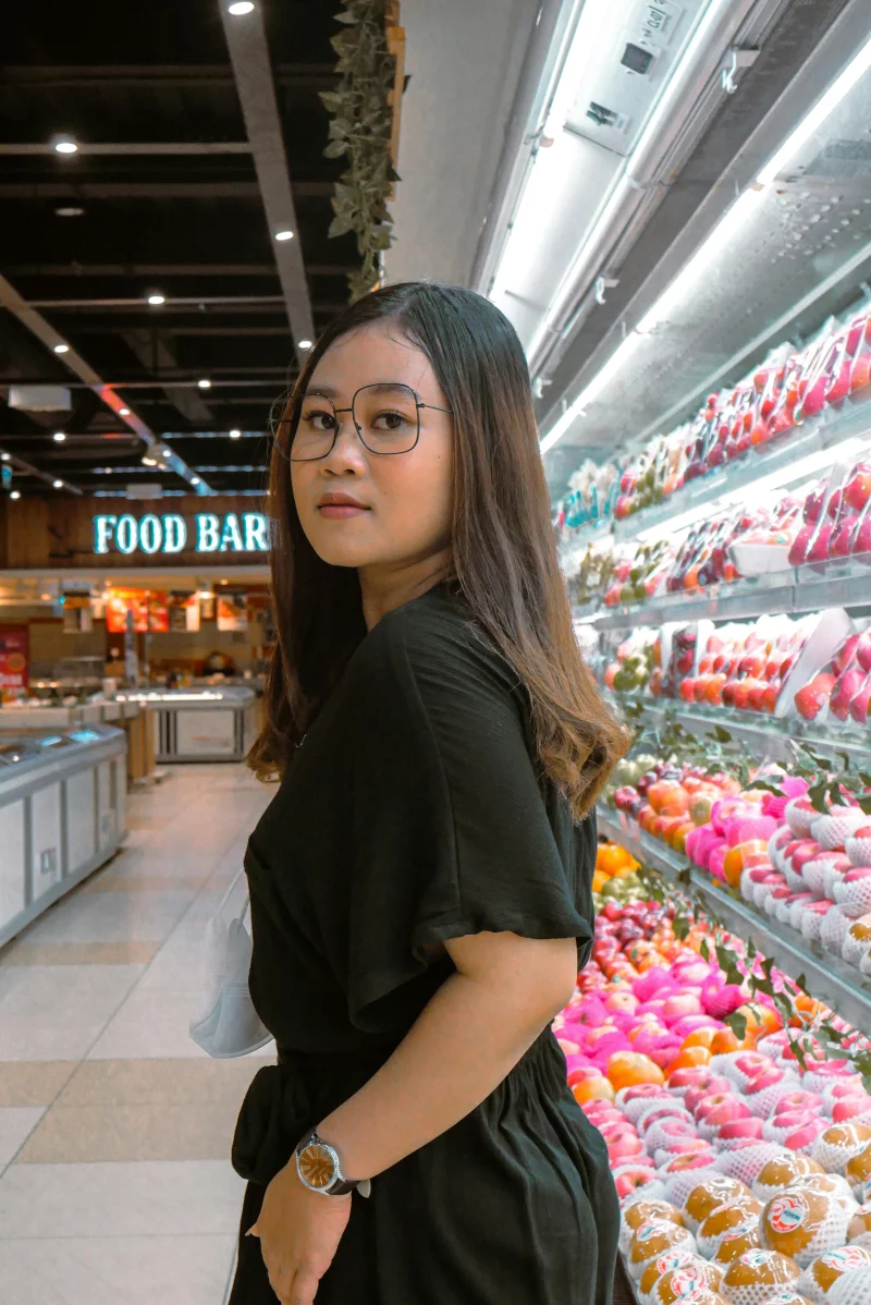 Young woman shopping in a supermarket with fresh fruits arranged on shelves.