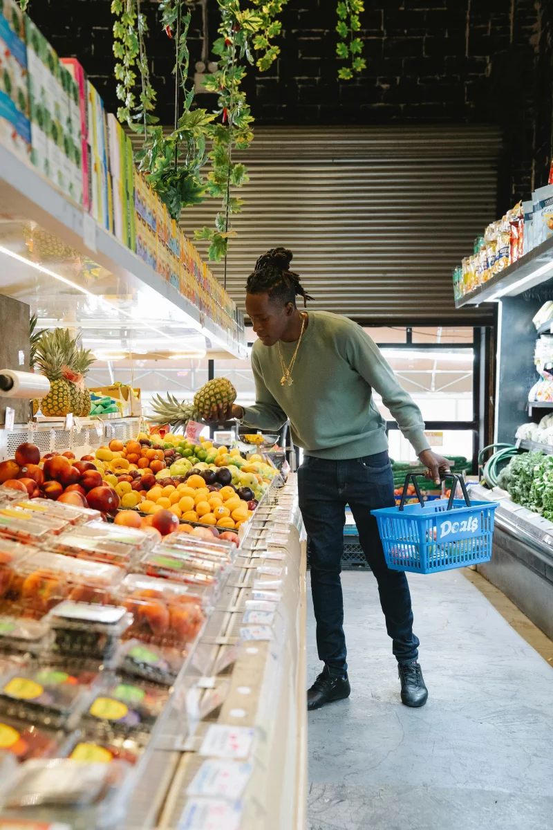 Adult man choosing fresh fruits at an indoor grocery store with a shopping basket.