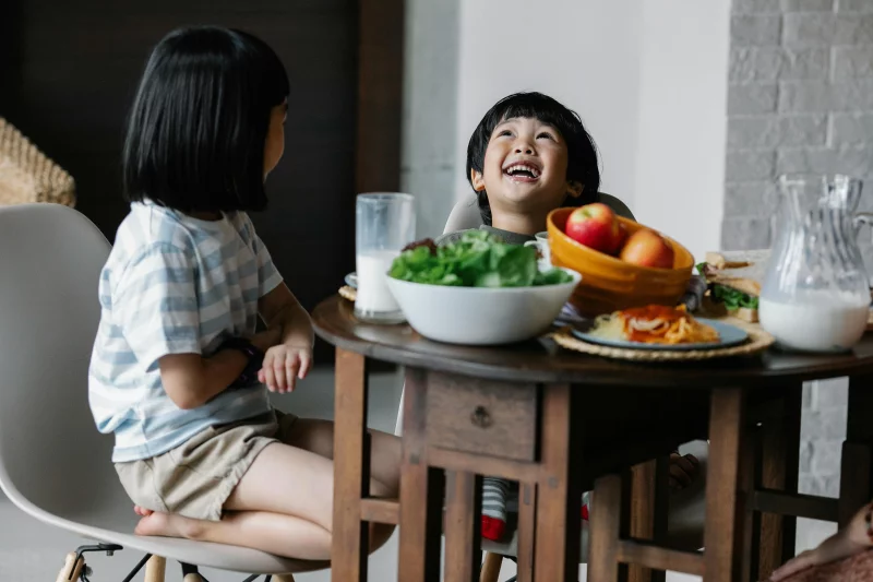 Two happy children enjoying a healthy meal at home, sharing laughter and nutritious food.