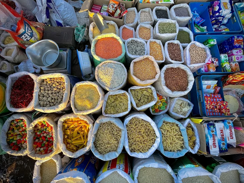 Top-down view of colorful market goods including spices, grains, and pasta in bags, showcasing a vibrant array of choices.