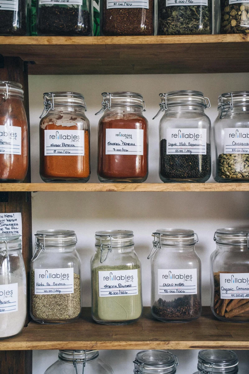 Organized eco-friendly glass jars filled with various spices on a wooden shelf for sustainable food storage.