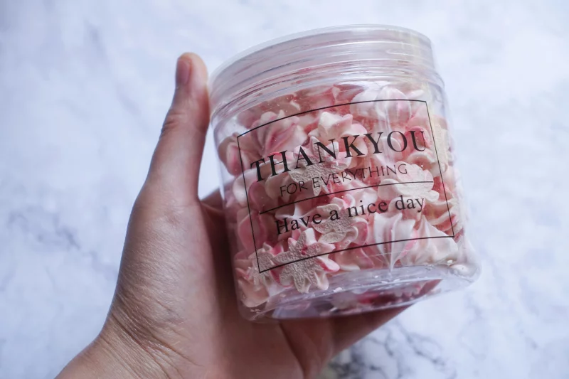 Close-up of a hand holding a jar of pink meringue cookies with a 'Thank you' message.