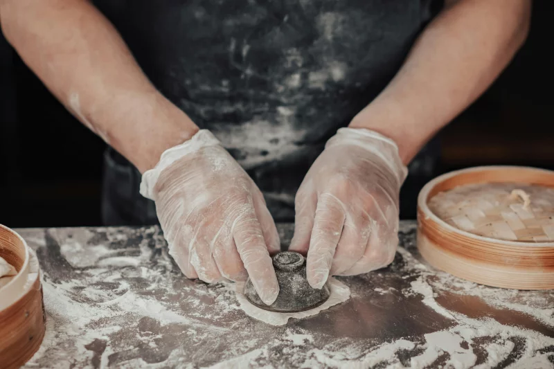 Close-up of hands skillfully crafting dough for dumplings using traditional tools in a kitchen setting.