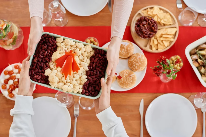 Top view of a festive table setting with a shared vegetable dish featuring beans and cauliflower.