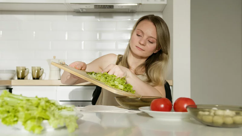 A woman preparing a fresh salad with lettuce and tomatoes in a modern kitchen.